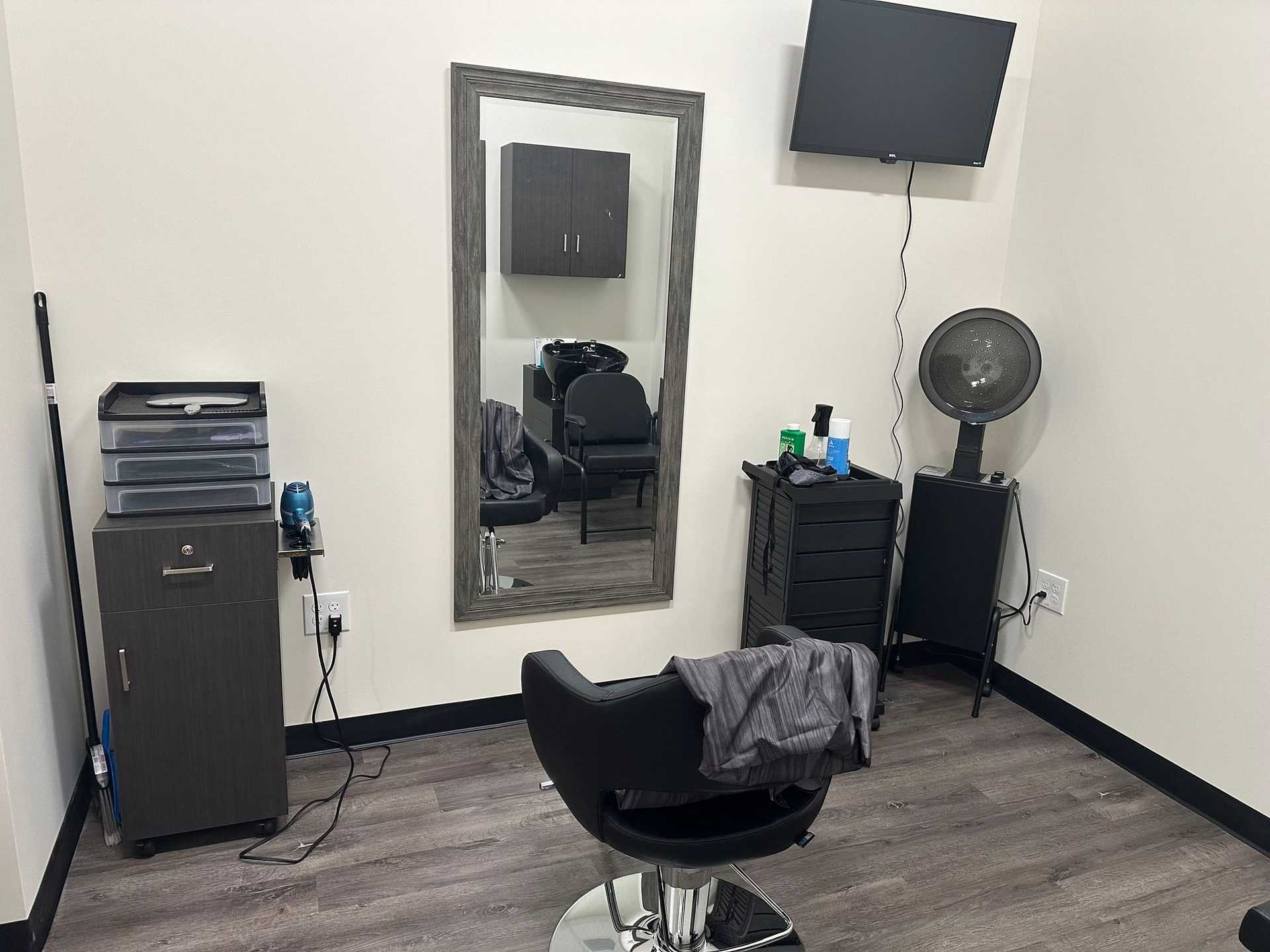 Small hair salon with a chair, mirror, cabinets, hairdryer, and a wall-mounted TV.